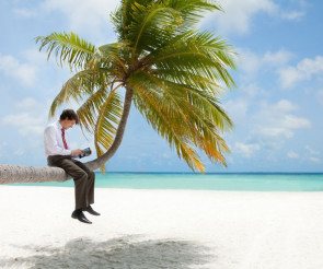 Mann in Krawatte sitzt mit Tablet auf einer Palme am Strand 