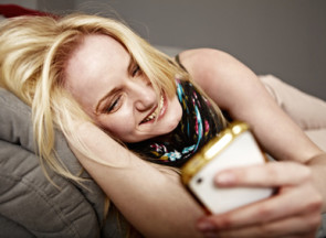Frau liegt auf Sofa und vergnügt sich mit Handy 