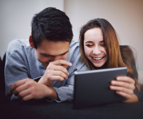 Zwei Menschen lachen und blicken auf Tablet 