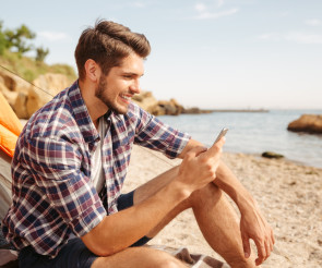 Ein Mann sitzt mit Smartphone in der Hand am Strand 