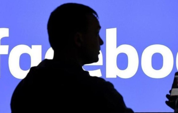 Mann steht vor Facebook-Logo 