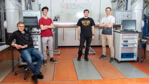 Die Physiker Philipp Kurpiers, Paul Magnard, Josua Schär und Simon Storz (von links nach rechts) vor der Quantenverbindung. Rechts und links im Hintergrund sind die beiden Kryostaten zu sehen.