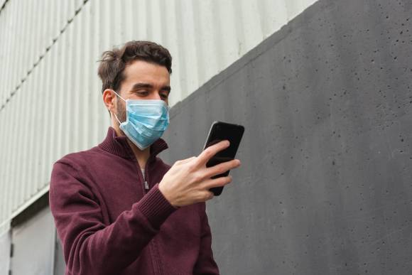Mann mit Mundschutz und Smartphone 