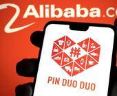 Pinduoduo Logo auf Smartphone, im Hintergrund Alibaba Logo