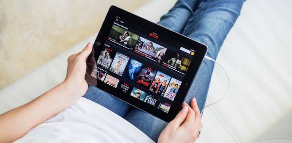 Person liegt mit iPad auf Couch und streamt Filme 