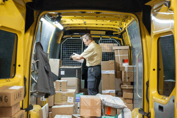 Ein Post-Angestellter in einem Post-Lieferwagen, umgeben von Paketen 