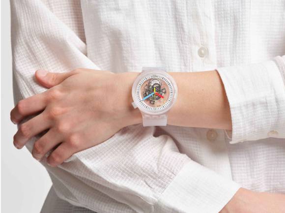Der Ausschnitt zeigt eine transparente Swatch am Handgelenk einer Frau in einer weissen Bluse 