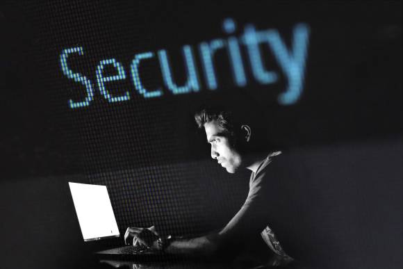 Mann am Laptop, Schriftzug Security, dunkler Hintergrund 