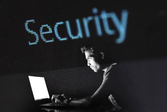 Mann am Laptop, Schriftzug Security, dunkler Hintergrund 