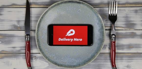 Delivery Hero App aus Smartphone, im Hintergrund Teller und Besteck 