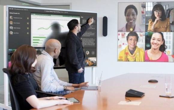 Symbolbild zeigt Konferenzraum mit Teams-Teilnehmenden auf der Leinwand 