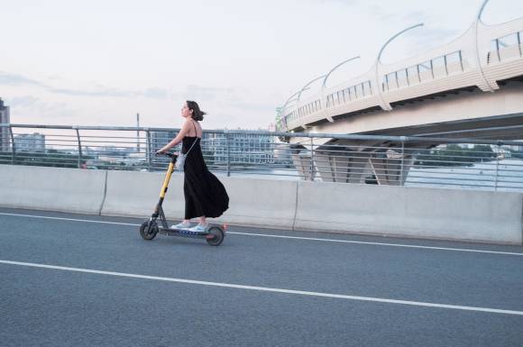 Eine Frau in schwarzem Kleid auf einem gelb-schwarzen E-Scooter 