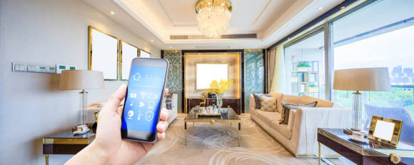 Smartphone zeigt Smart-Home-Icons, in der Hand einer Person, die in einer schicken Wohnung steht 
