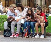 Vier Mädchen sitzen nebeneinander auf einen Bank und schauen auf ihre Smartphones
