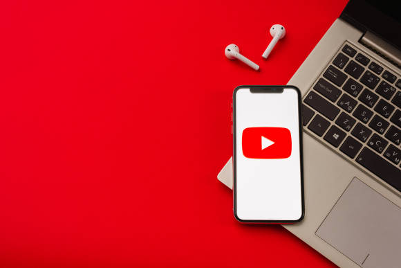 Ein Smartphone zeigt ein YouTube-Logo und liegt auf einem aufgeklapptem Notebook 