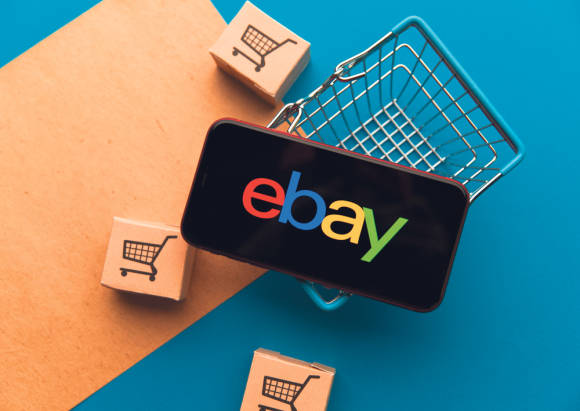 Symbolbild zeigt ein eBay-Logo, umgeben von Einkaufswagen-Symbolen