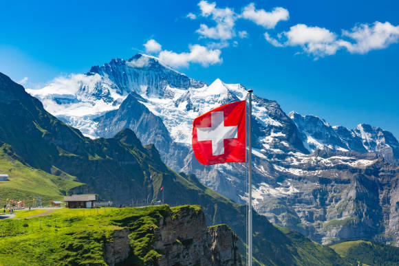 Symbolbild zeigt Schweizer Fahne. Im Hintergrund die Alpen. 