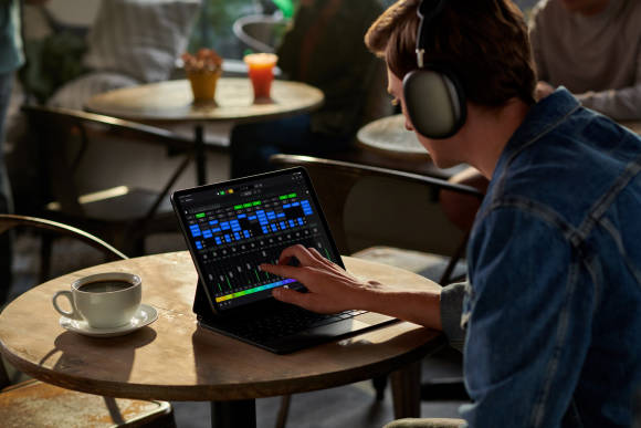 Ein Musiker sitzt in einem Kaffee vor dem iPad Pro, auf dem die App Logic Pro läuft 