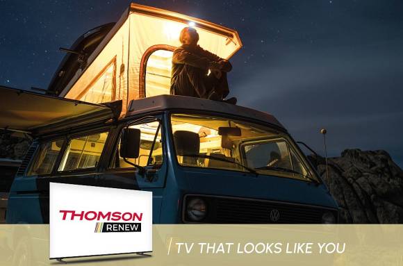 Thomson-TV-Banner zeigt Mann, der nachts auf dem Dach seines Campers sitzt 