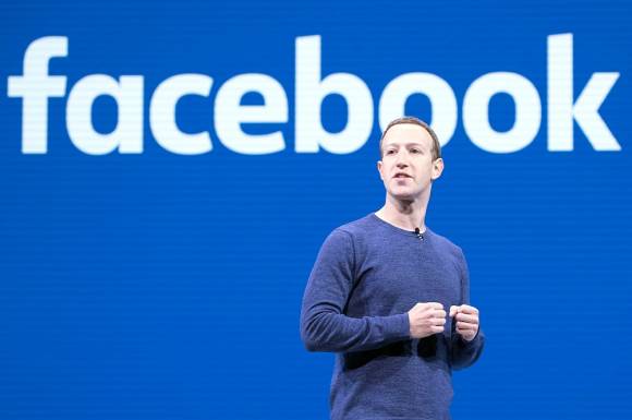 Mark Zuckerberg steht vor einer Wand mit Facebook-Logo 