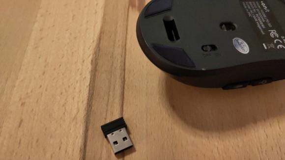 Die Maus liegt auf dem Rücken, man sieht den leeren Dongle-Steckplatz,daneben liegt der kleine USB-Dongle