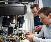 Zwei Mitarbeiter des Fraunhofer AISEC prüfen elektronische Bauteile mit Spezialgeräten auf Herz und Nieren