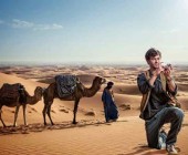 Mann kniet in der Wüste vor Kamelen mit einer Kamera in der Hand
