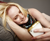 Frau liegt auf Sofa und vergnügt sich mit Handy