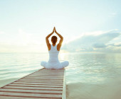 Eine Frau sitzt auf einem Steg und macht Yoga