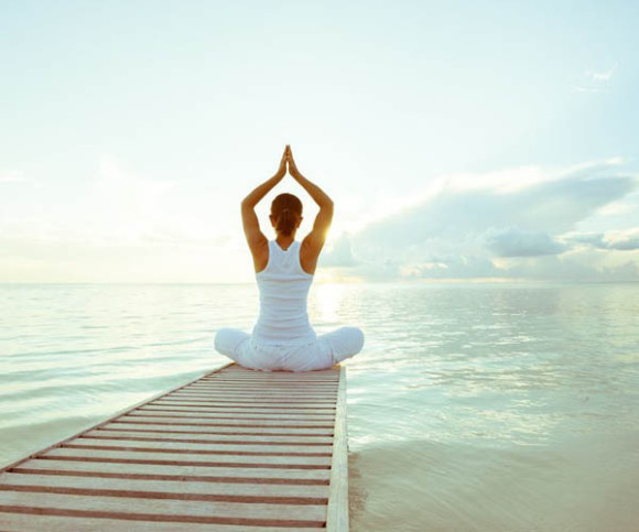 Eine Frau sitzt auf einem Steg und macht Yoga 