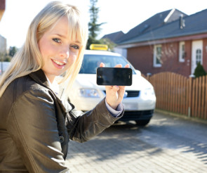 Frau hält ein Smartphone in der Hand und sitz vor einem Auto 