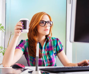 Frau sitzt mit Kaffee in der Hand am Desktop-PC 