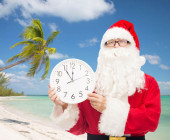 Weihnachtsmann am Strand mit Palme mit weißer Uhr in der Hand