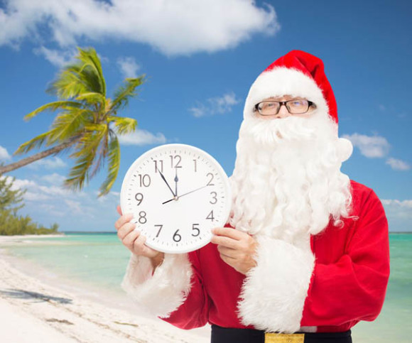 Weihnachtsmann am Strand mit Palme mit weißer Uhr in der Hand 