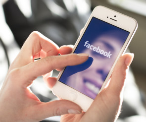 Frau hält ein Smartphone mit der Facebook App in der Hand 