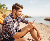 Ein Mann sitzt mit Smartphone in der Hand am Strand